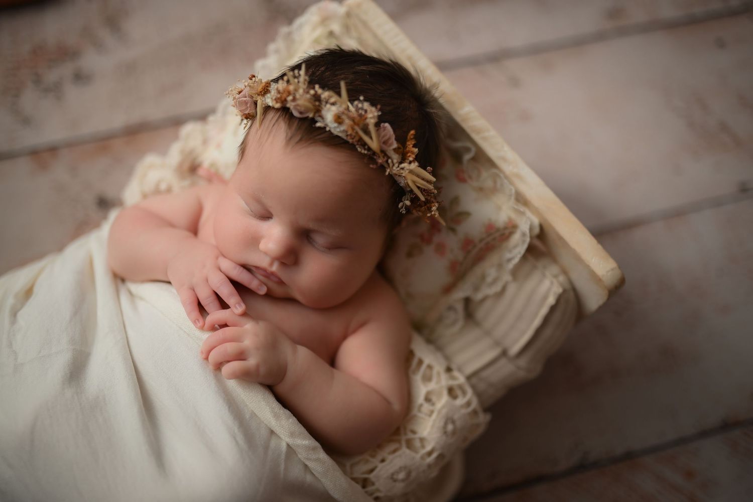 Sleeping newborn wearing delicate crown rests on soft lace bedding.