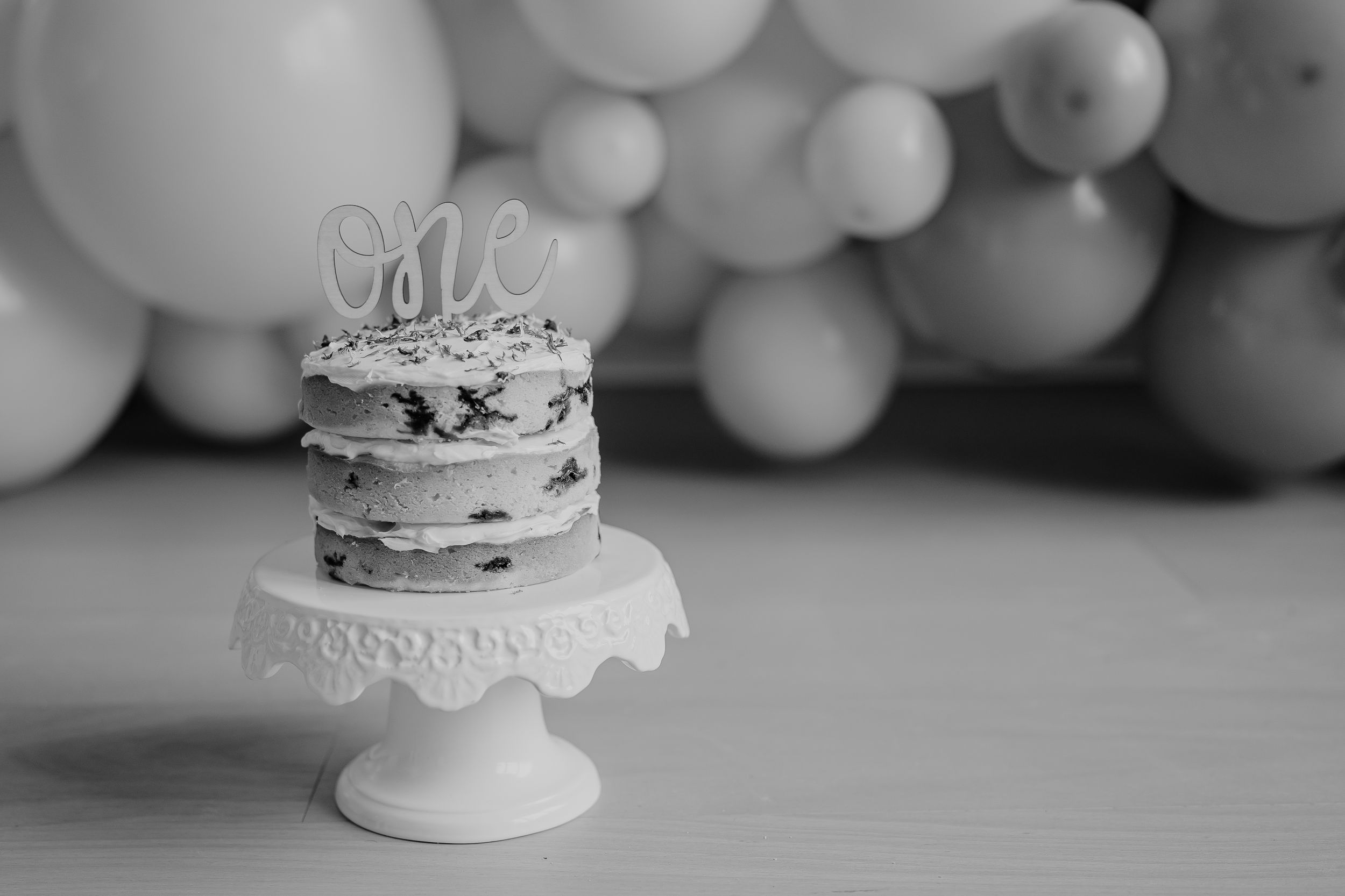 Black and white wedding cake photos showing elegant white tiers and decorative details against a balloon backdrop.