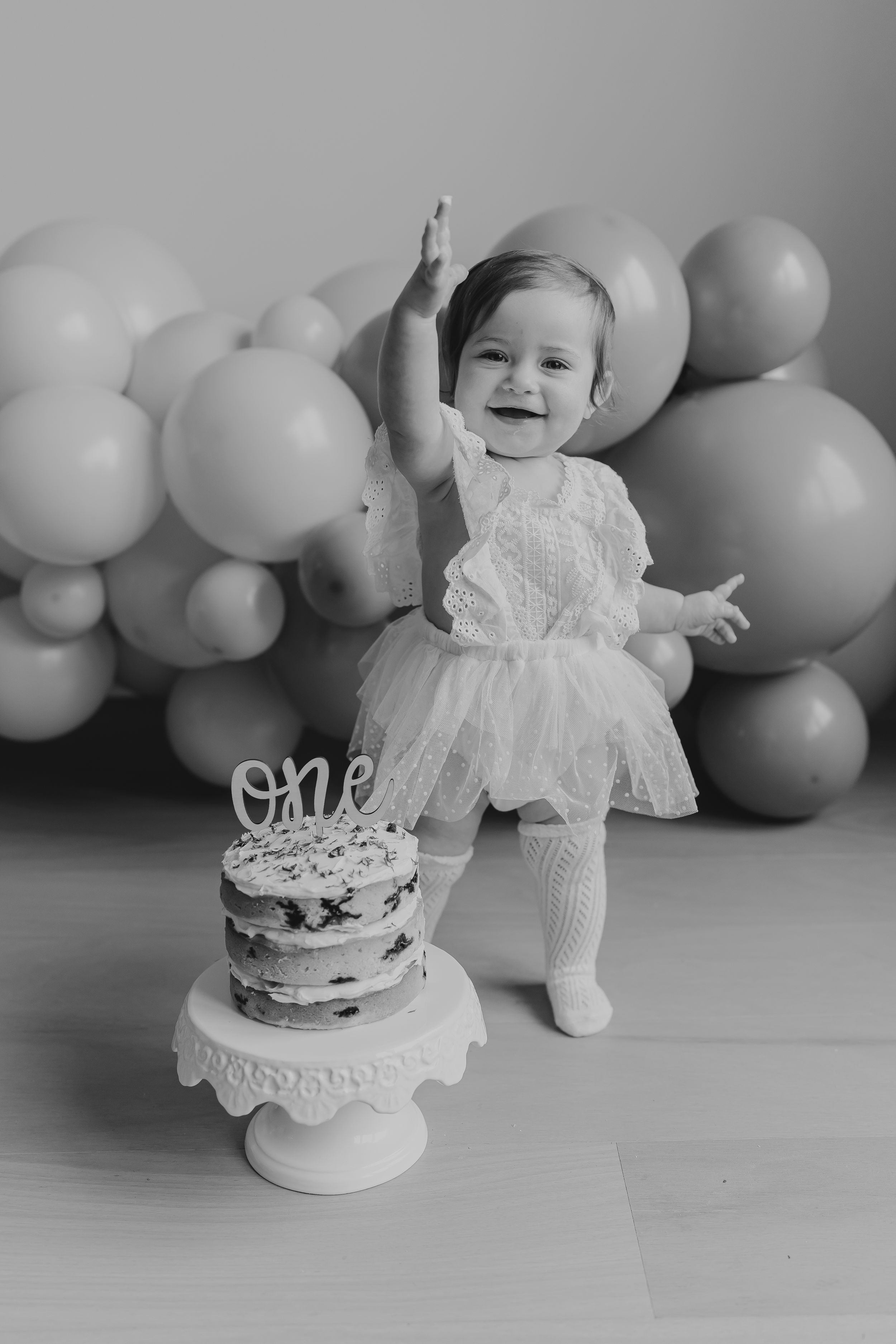 Black and white first birthday cake smash photo session with white balloons and lace dress decorations.