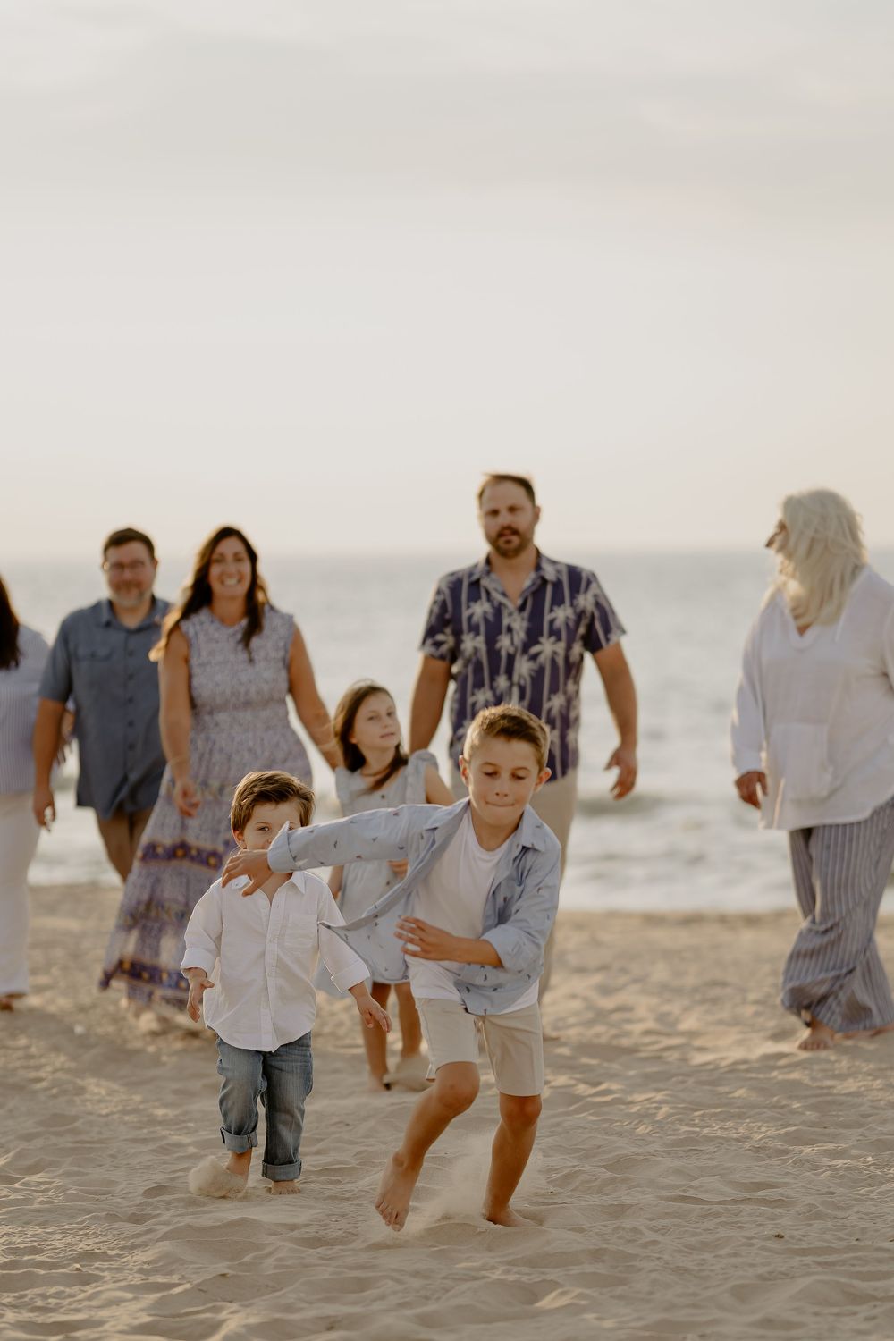 A group of people walking together joyfully along a sandy beach at sunset in casual summer attire.