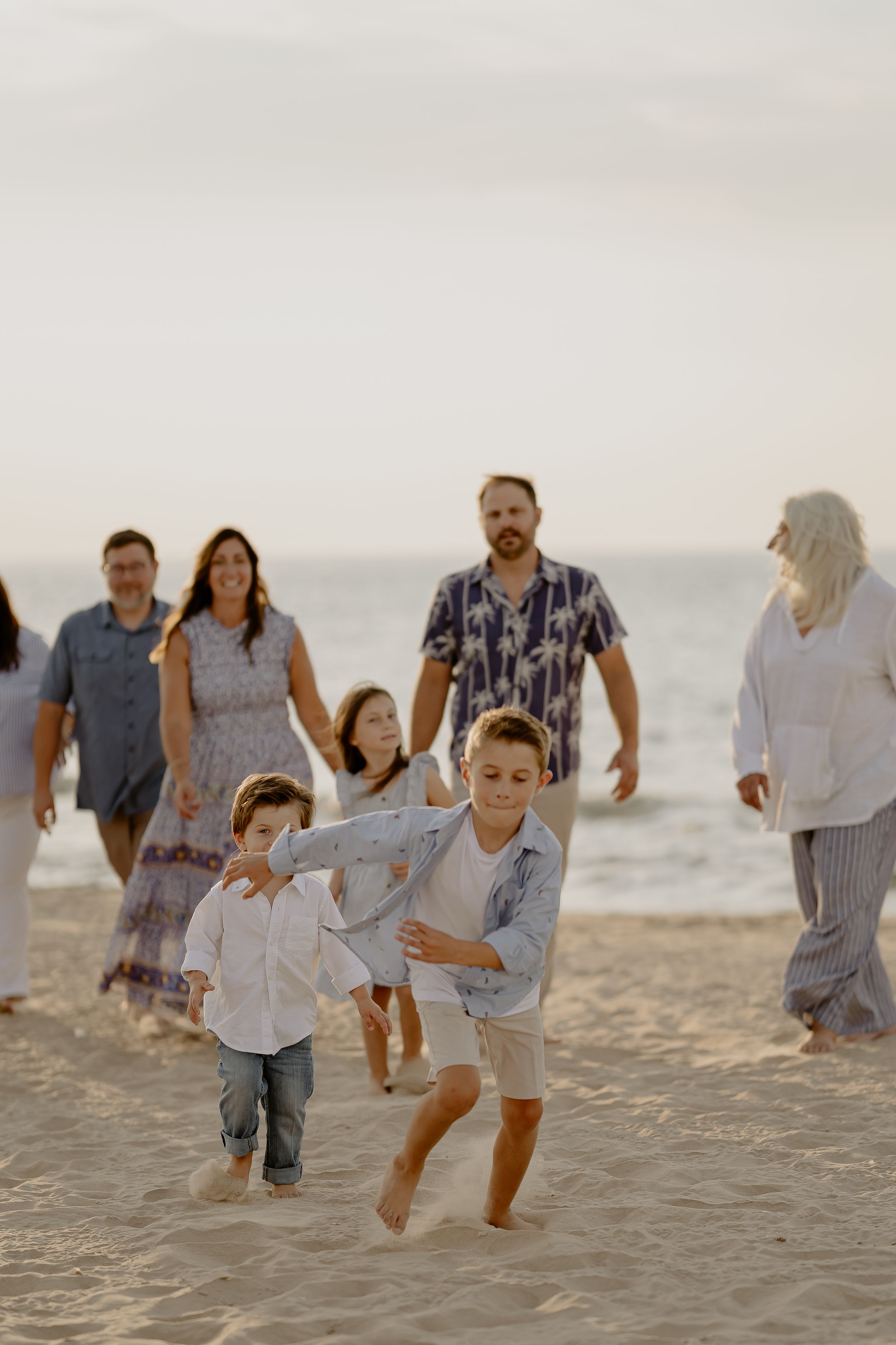 A group of people walking together joyfully along a sandy beach at sunset in casual summer attire.