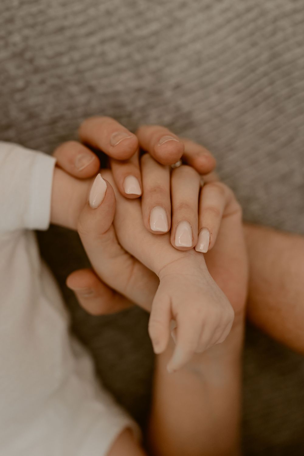 Close-up shot of hands with white manicured nails gently clasped together against a soft gray background.