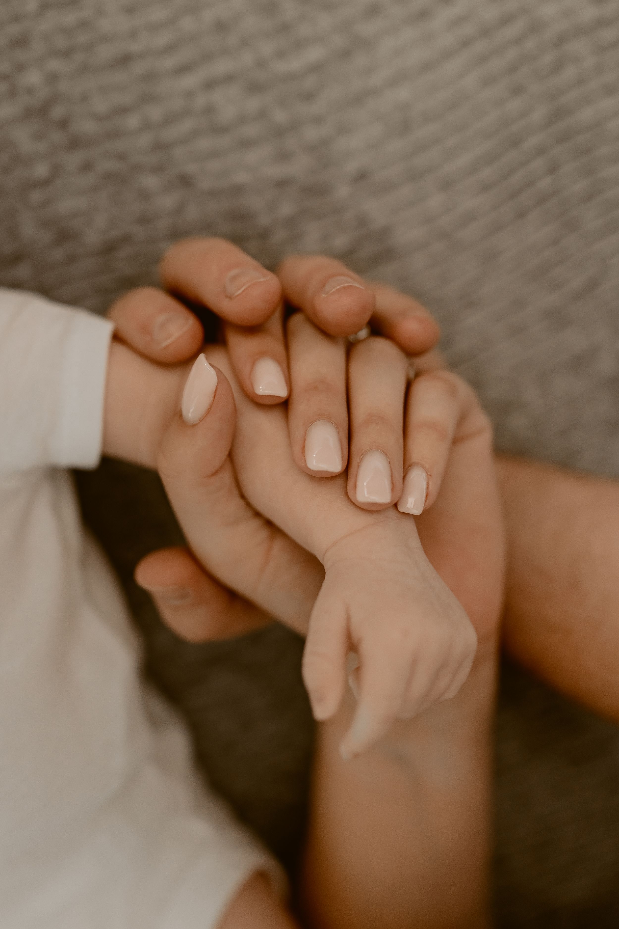 Close-up shot of hands with white manicured nails gently clasped together against a soft gray background.