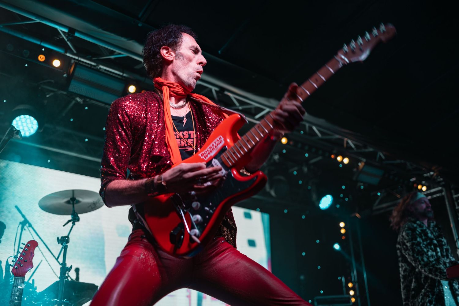 Guitarist in red outfit playing electric guitar on stage with teal and blue lighting, live music event photography Southampton