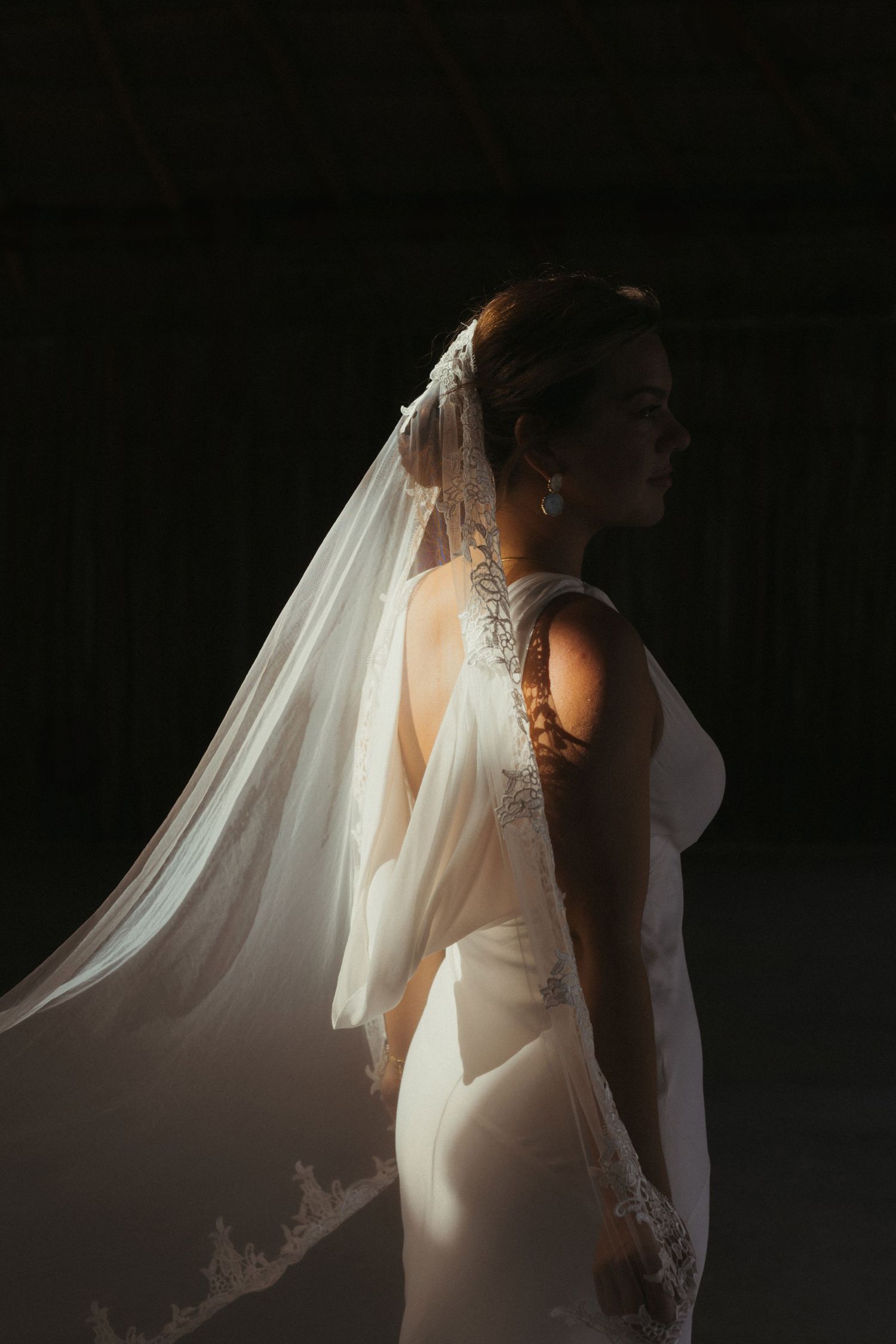 Dramatic side-lit bridal portrait showing intricate lace veil details against dark background. Wedding photographer in Mexico Riviera Maya