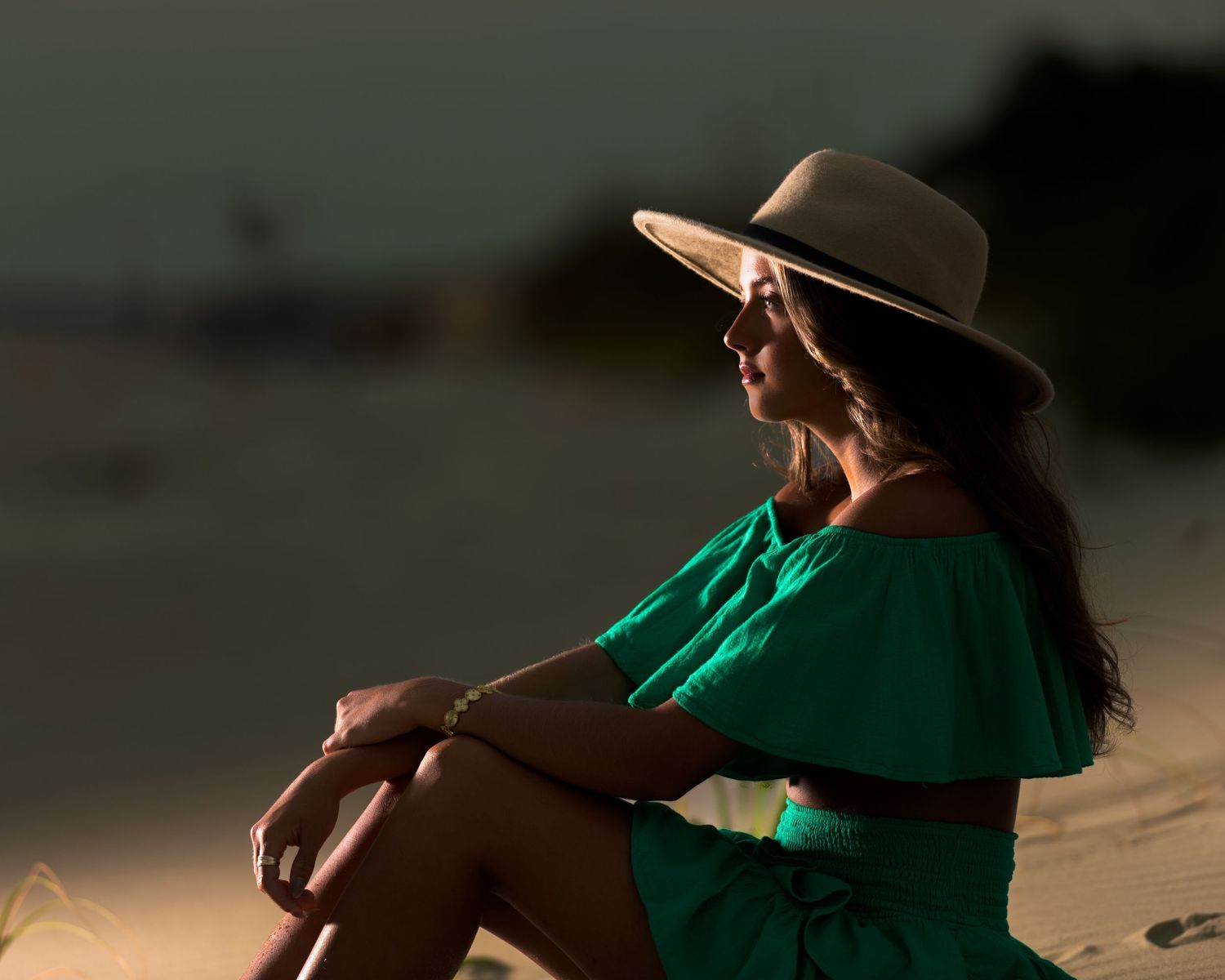Woman in green dress and sun hat sitting on beach at sunset. Myrtle beach photographer