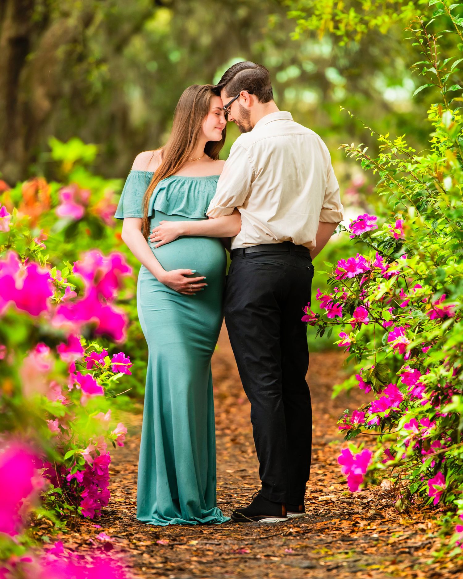 A couple shares an intimate moment in a garden path framed by vibrant pink bougainvillea flowers and lush greenery. Charleston Photographer