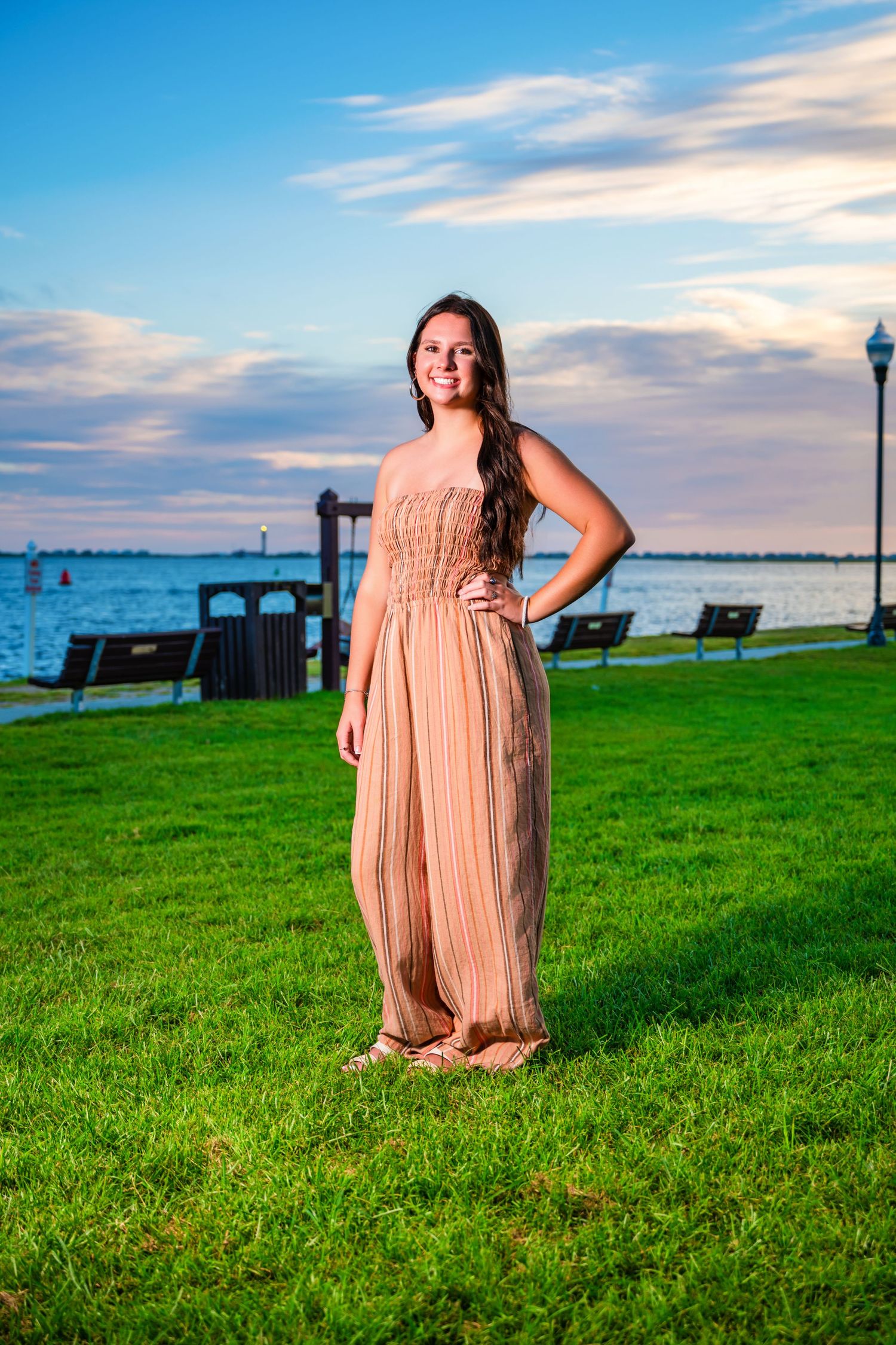 Person in peach maxi dress standing on grassy waterfront at sunset. Myrtle beach photographer