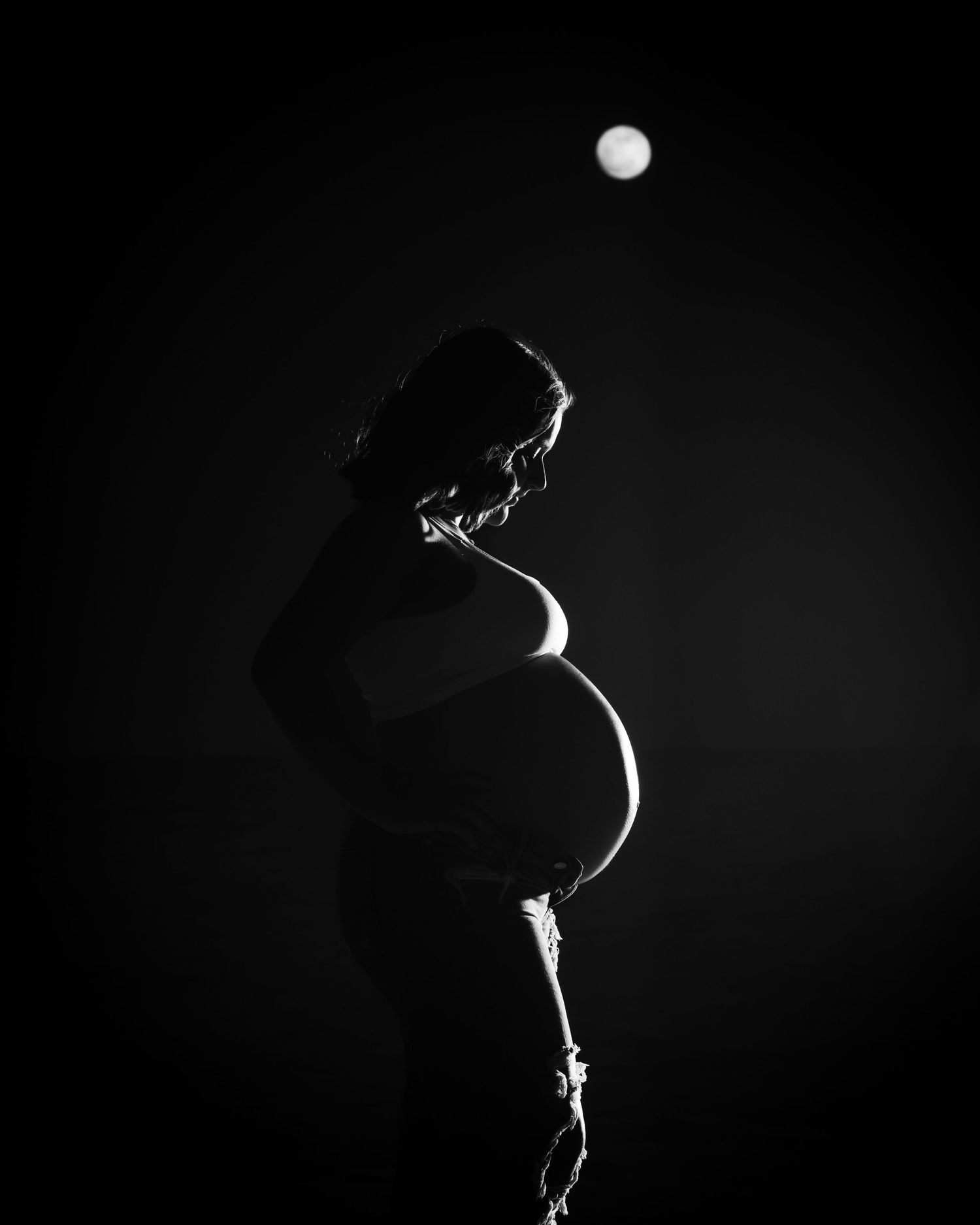 Artistic silhouette of pregnant woman with moon in night sky. Myrtle beach photographer