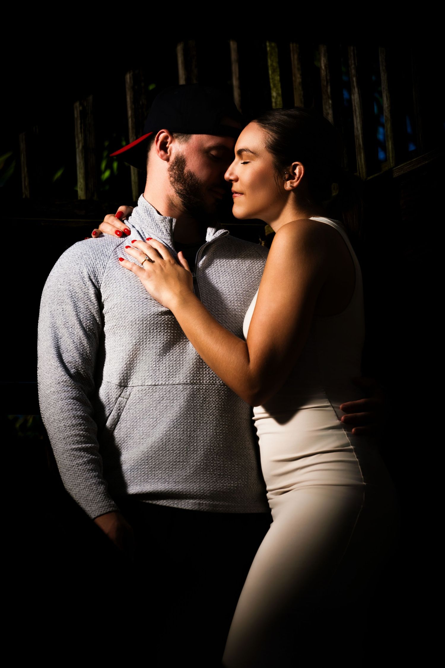An intimate couple's portrait with dramatic lighting against a dark wooden fence. Myrtle beach photographer