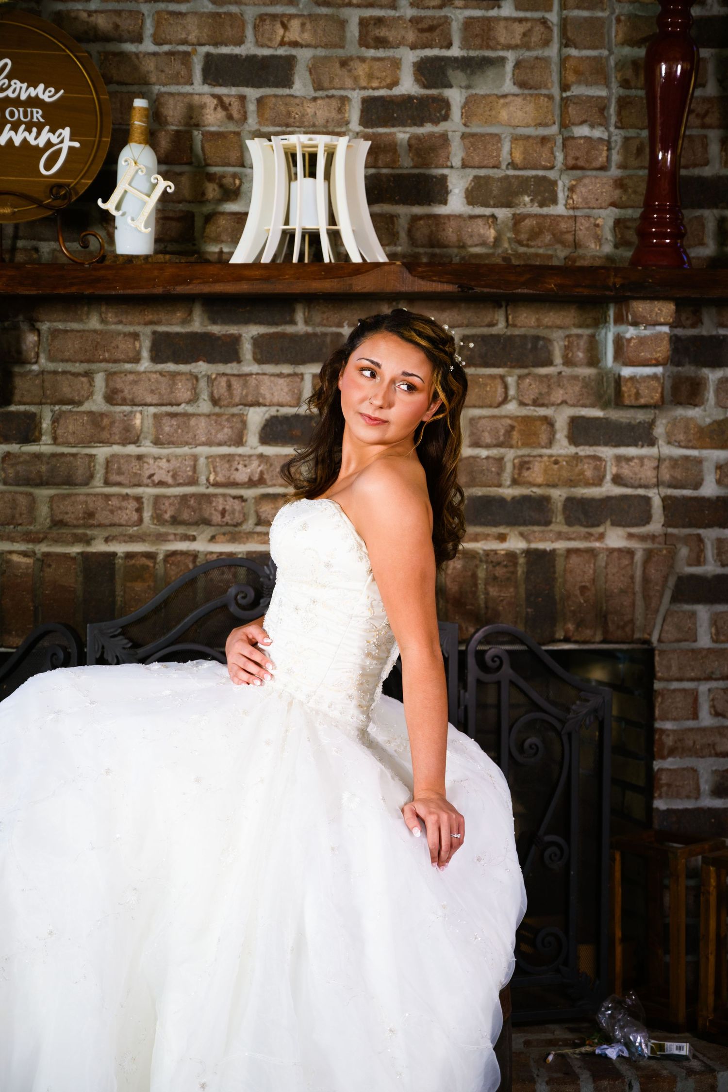 White wedding gown against rustic brick backdrop with home decor on mantle. Myrtle beach photographer