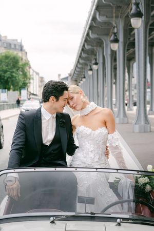 Romantic moment captured in vintage car on iconic Parisian bridge.
