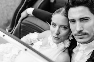 Black and white portrait of newlyweds posing together in a vintage car.