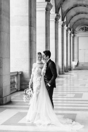 Black and white wedding portrait under classical columned arcade at historic Parisian palace.