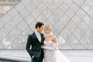 Elegant couple shares intimate moment in front of iconic Louvre pyramid in Paris.