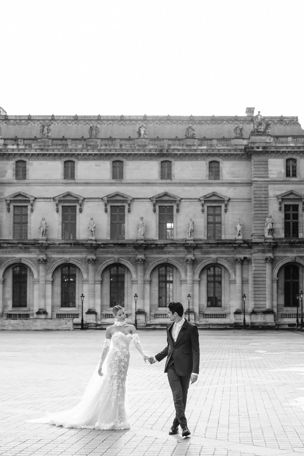 Black and white portrait of couple in formal attire against classical French architecture.