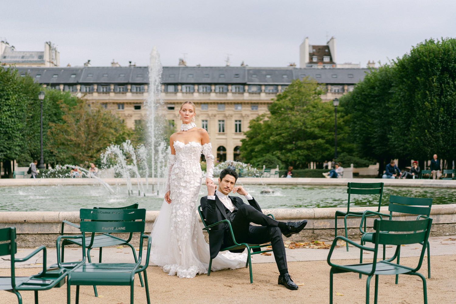Wedding couple poses in garden setting with ornate fountain and green chairs at Palais Royal.