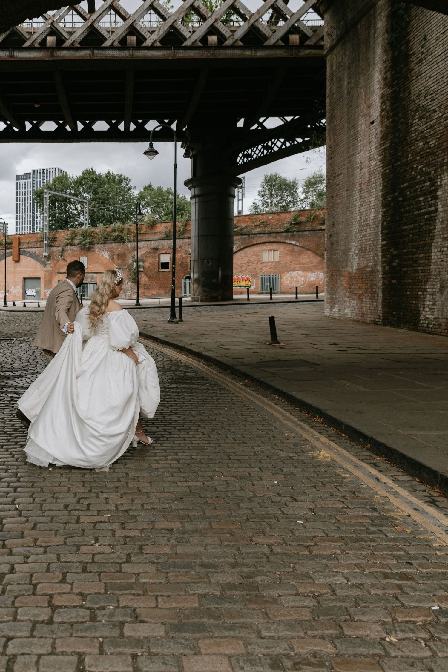 Low angle shot of couple walking together on wet city street showing white dress and dark pants.