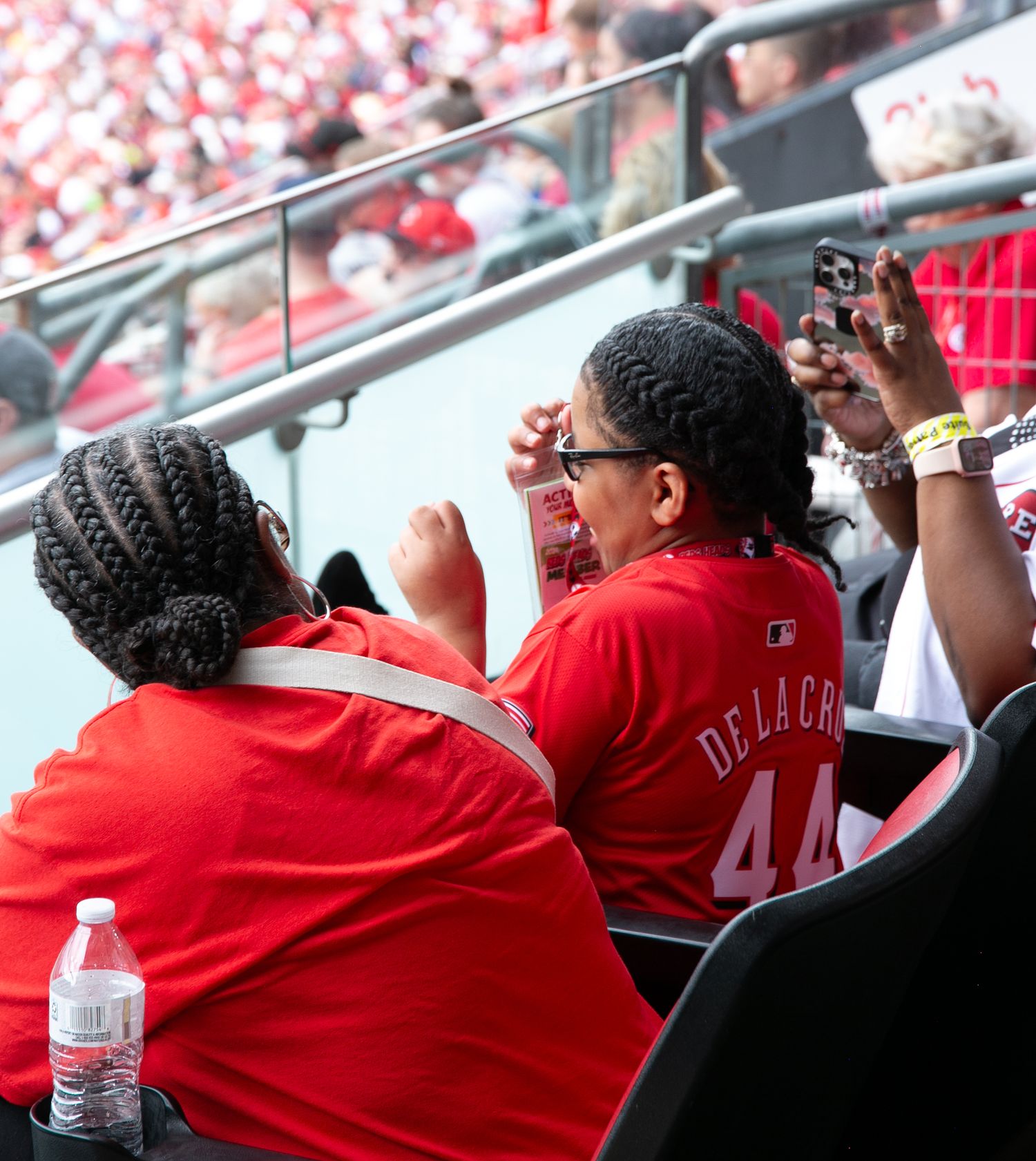 Baseball fans in red jerseys watching a game from stadium seats while enjoying refreshments.