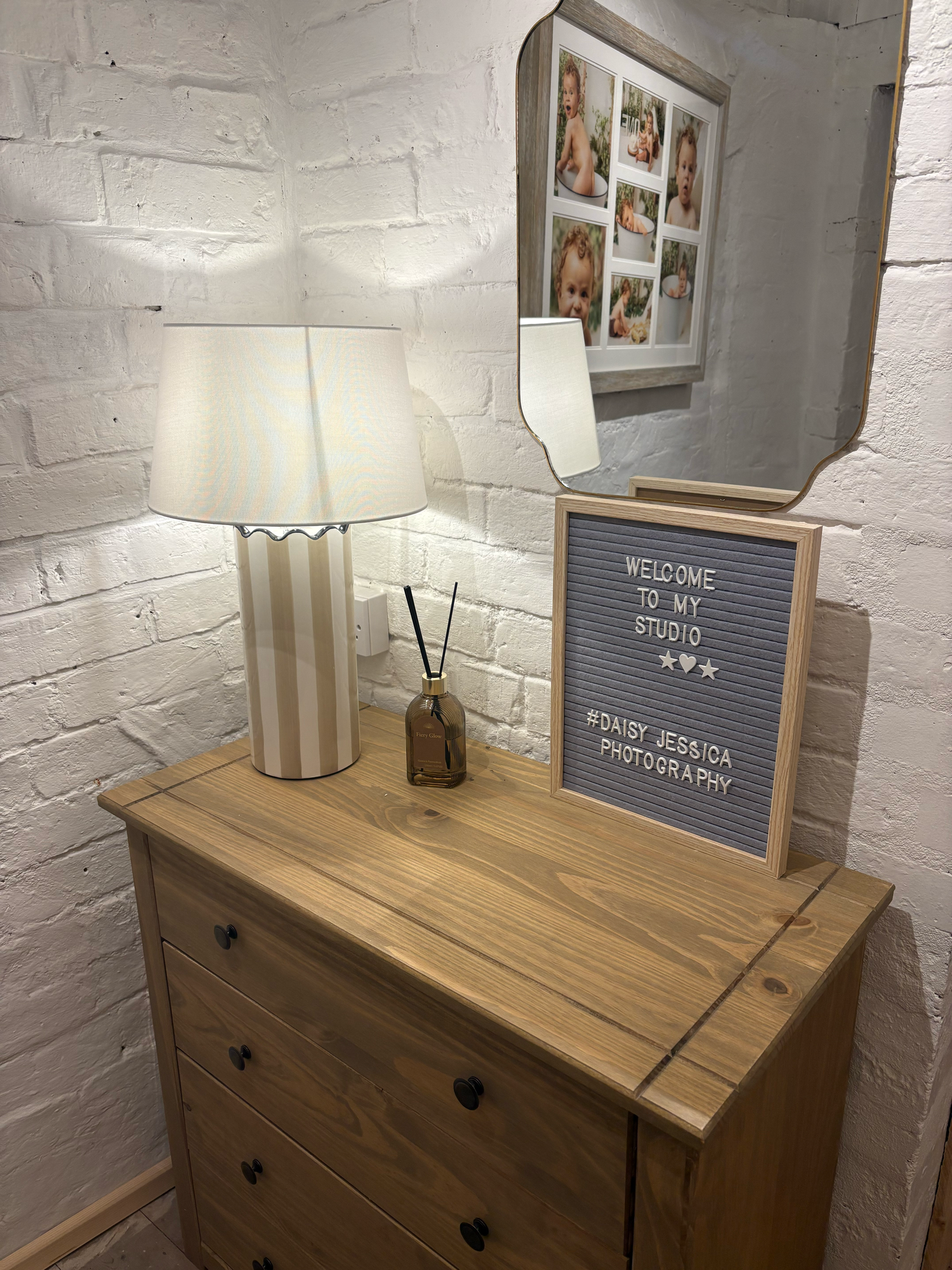 Cozy photography studio corner with wooden dresser, striped lamp, and welcome sign for Daisy Jessica Photography.