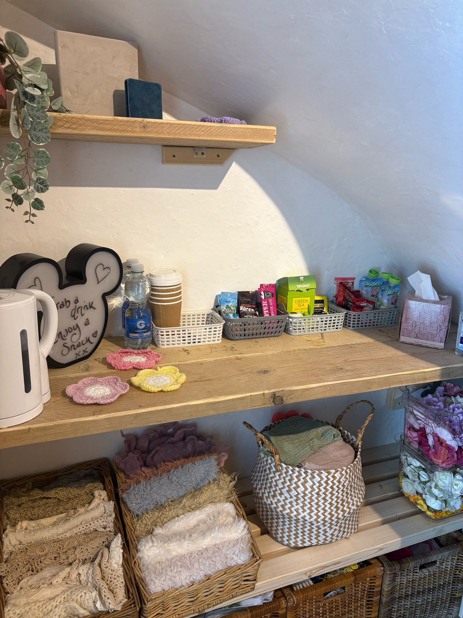 Rustic wooden shelving unit displaying tea station, folded towels, wicker baskets, and colorful spa products in a cozy salon.