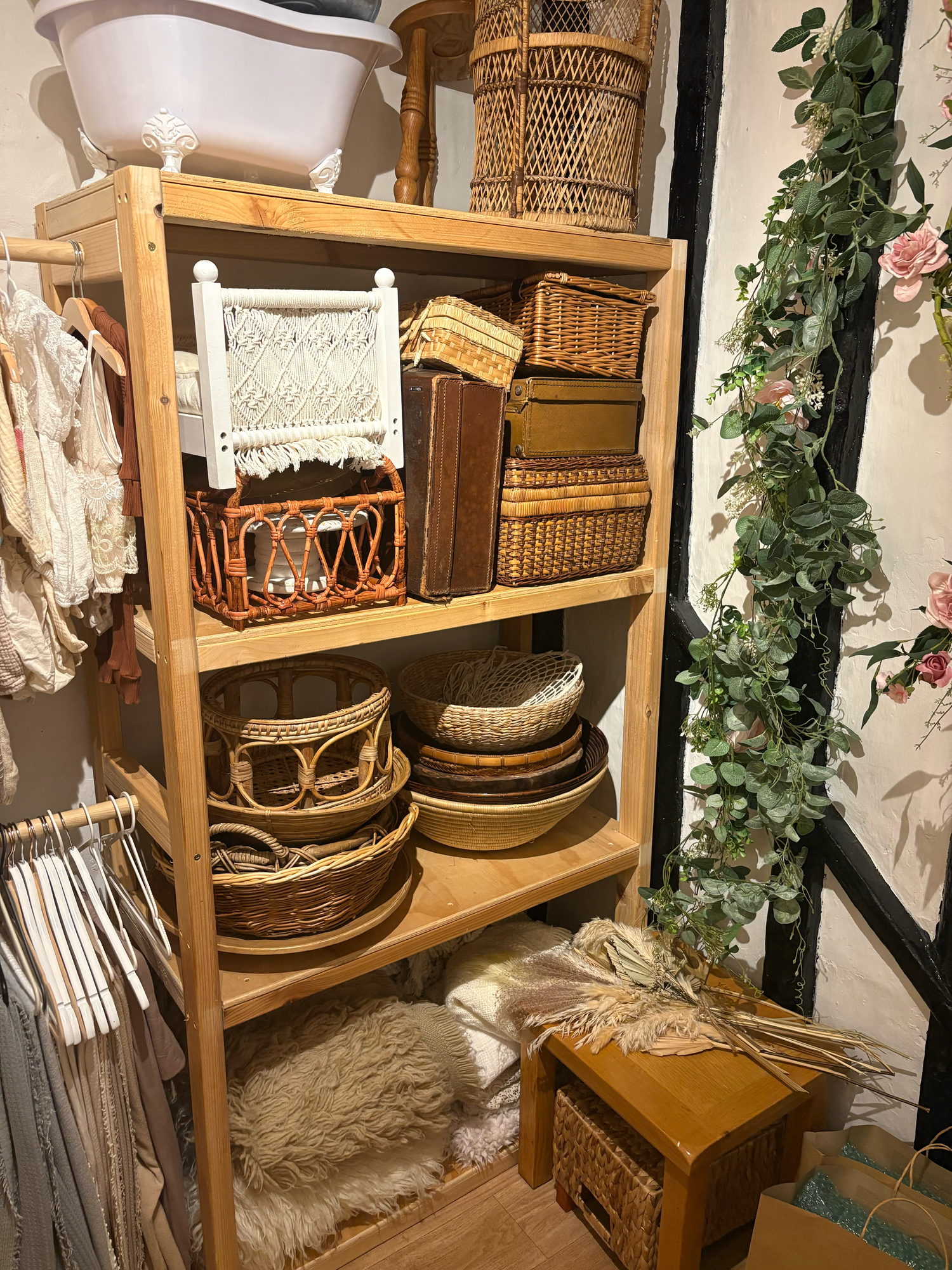 Wooden shelf displaying wicker baskets, rattan trays, and boho decor beside a faux ivy garland in a boutique shop.