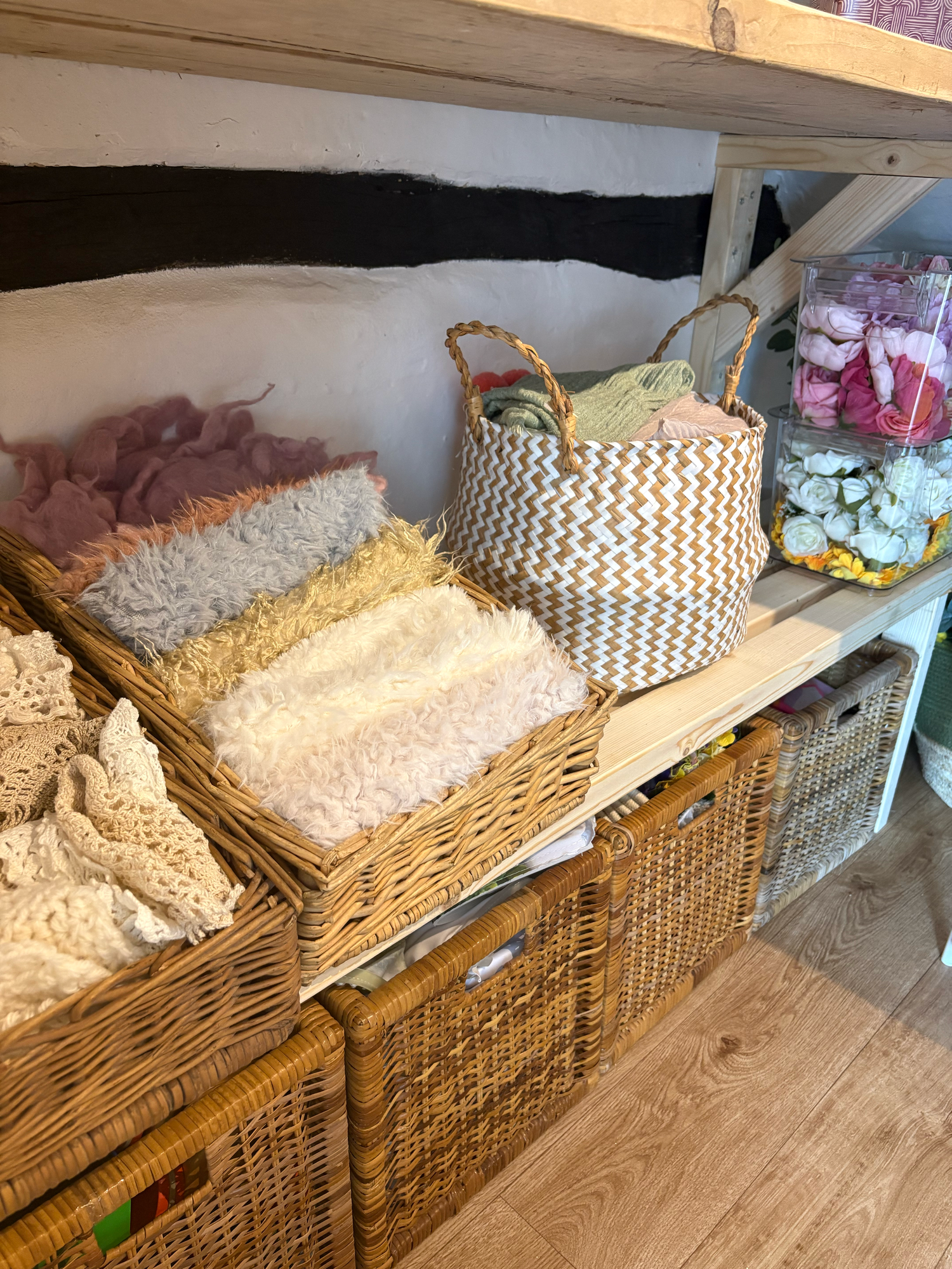 Wicker baskets filled with soft textured blankets and fabrics displayed on wooden shelves in a cozy craft store.