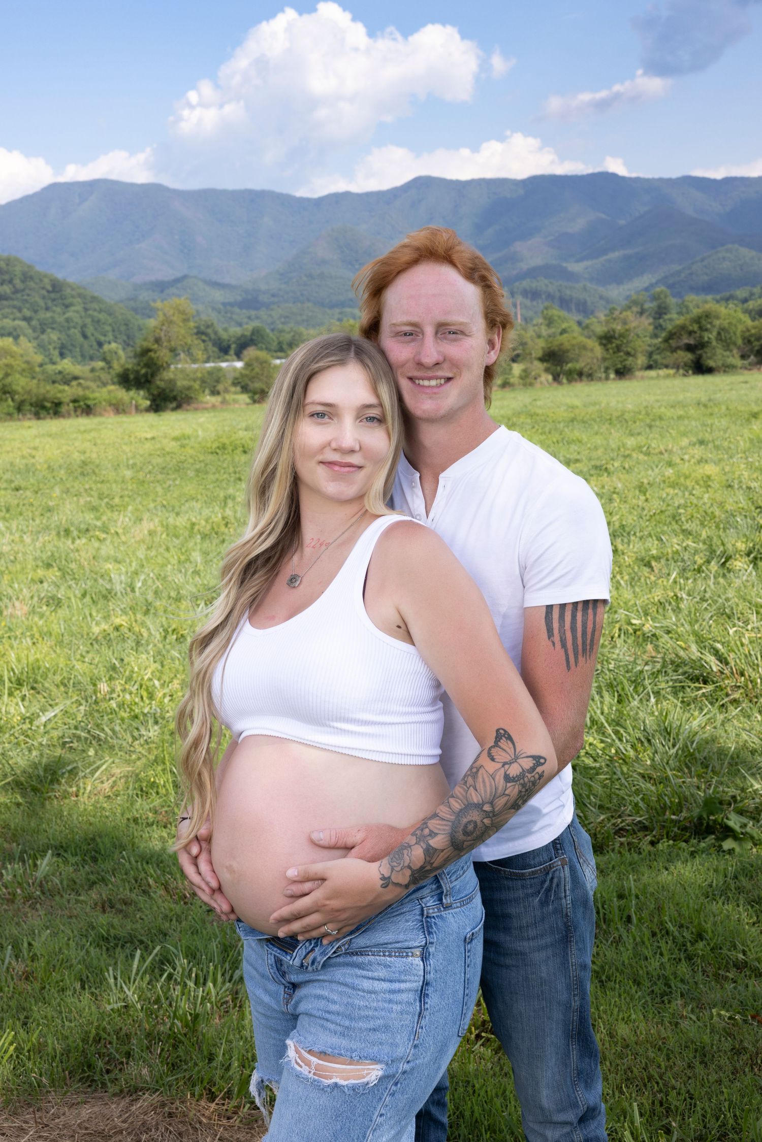 Couple's maternity photography session in mountain meadow on sunny day.