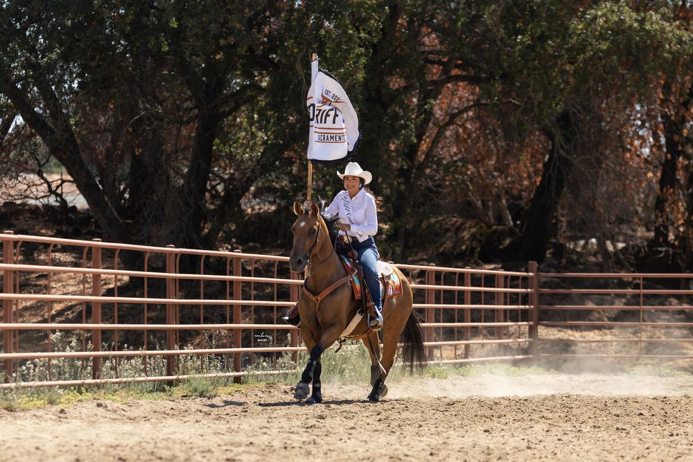 Cowgirl riding brown horse carrying a white flag in a dusty ranch arena. Queen-Jaylynn Lopez-Sacramento County Sheriffs Rodeo