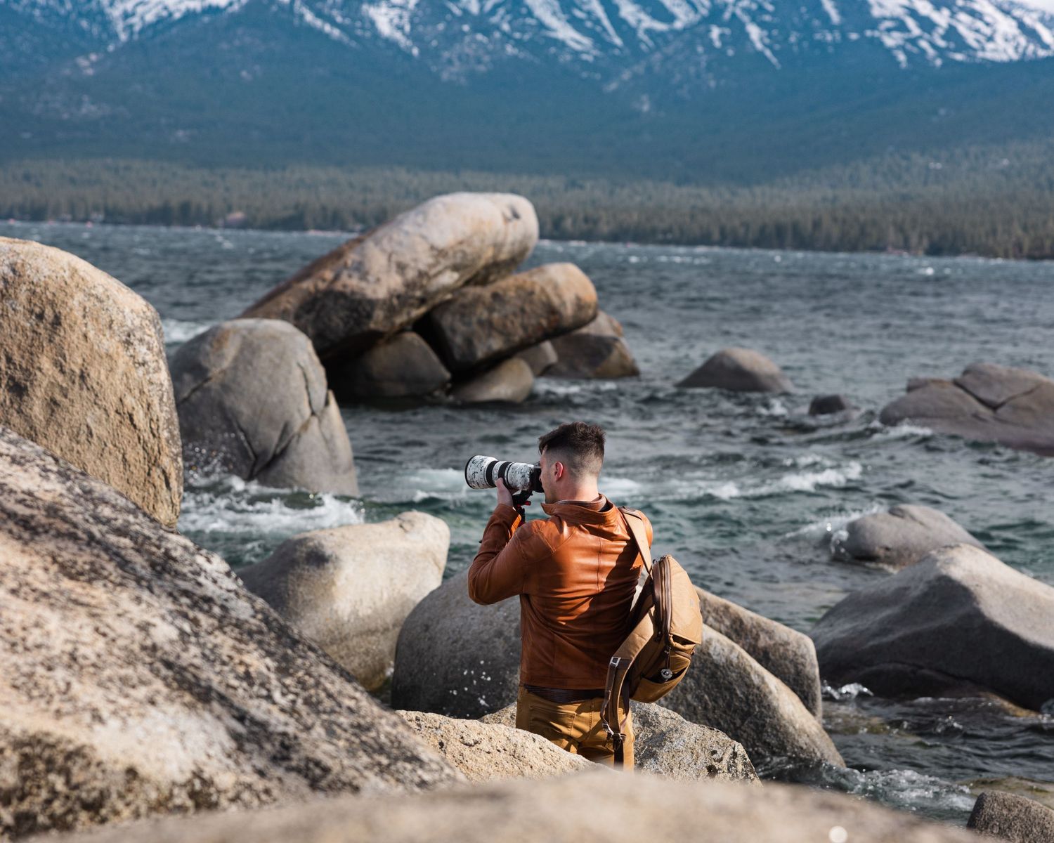 Photographer captures scenic mountain landscape with snow-capped peaks and rocky shoreline.