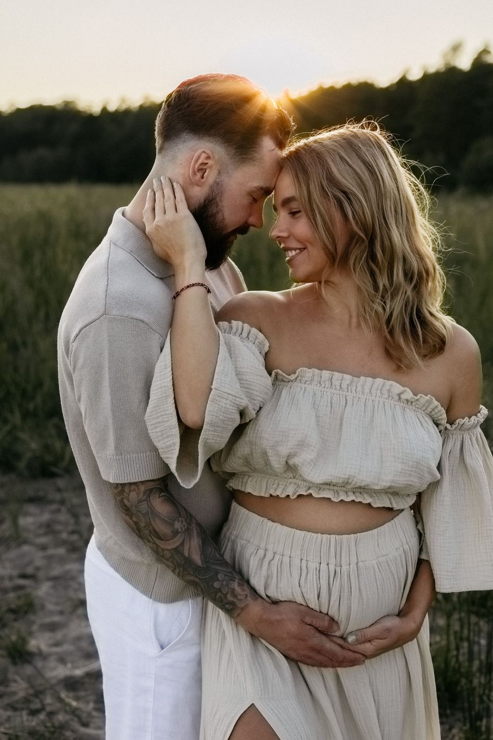 Intimate maternity photo of couple embracing in sunlit field at sunset.