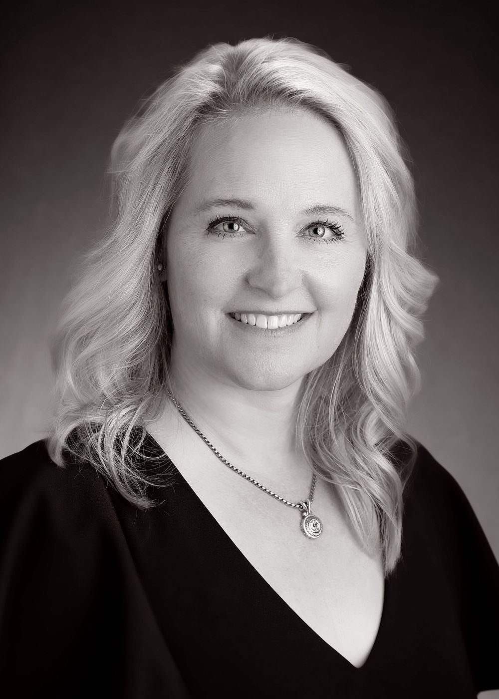 Professional black and white headshot portraits of a person with blonde hair wearing black against a dark background.