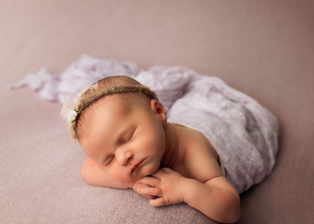 Peaceful newborn resting on soft beige fabric with delicate lace wrap and headband during portrait session.