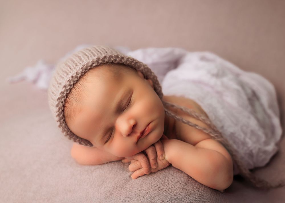 Artistic newborn portrait series with baby in delicate white wrap against beige background.