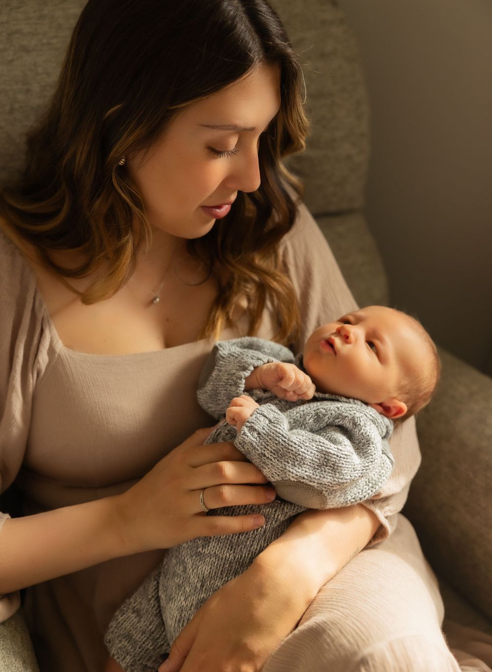 Intimate lifestyle portrait of mother and baby sharing a tender moment on grey couch in natural light.