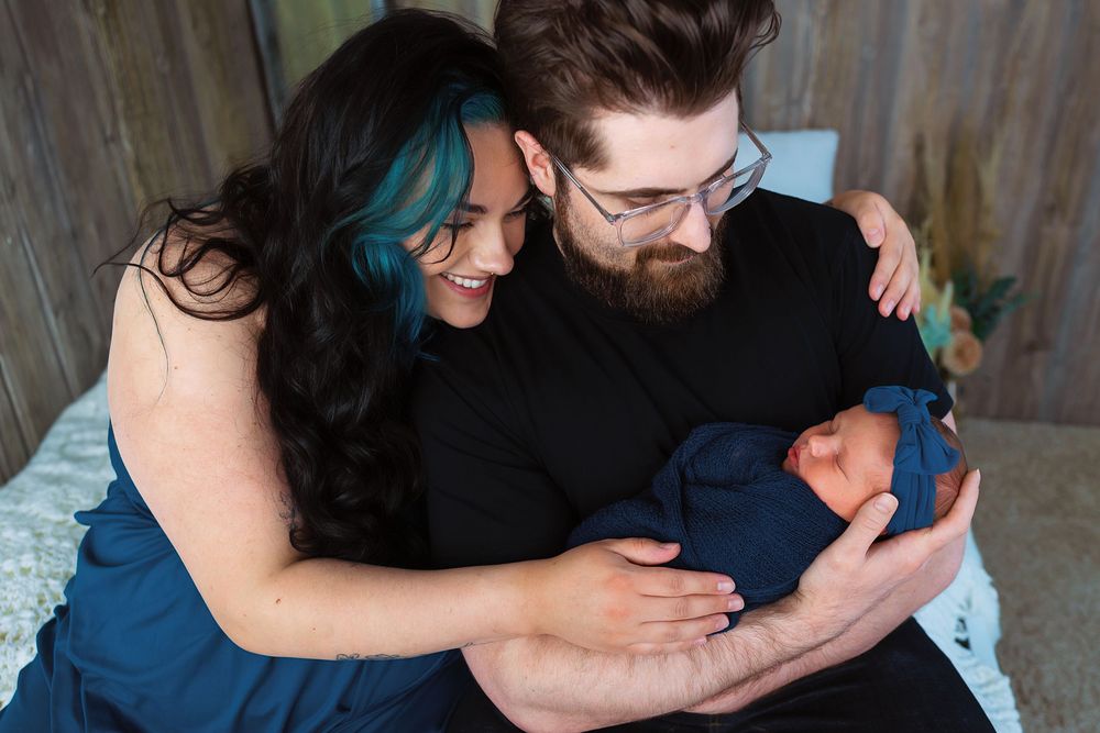 A couple embraces tenderly while holding their newborn baby in a series of intimate family photos.