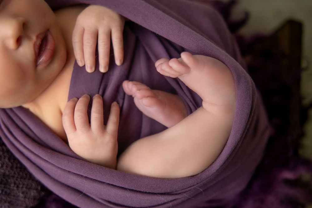 Close-up sequence showing a baby's tiny fingers and hands against a soft purple fabric background.