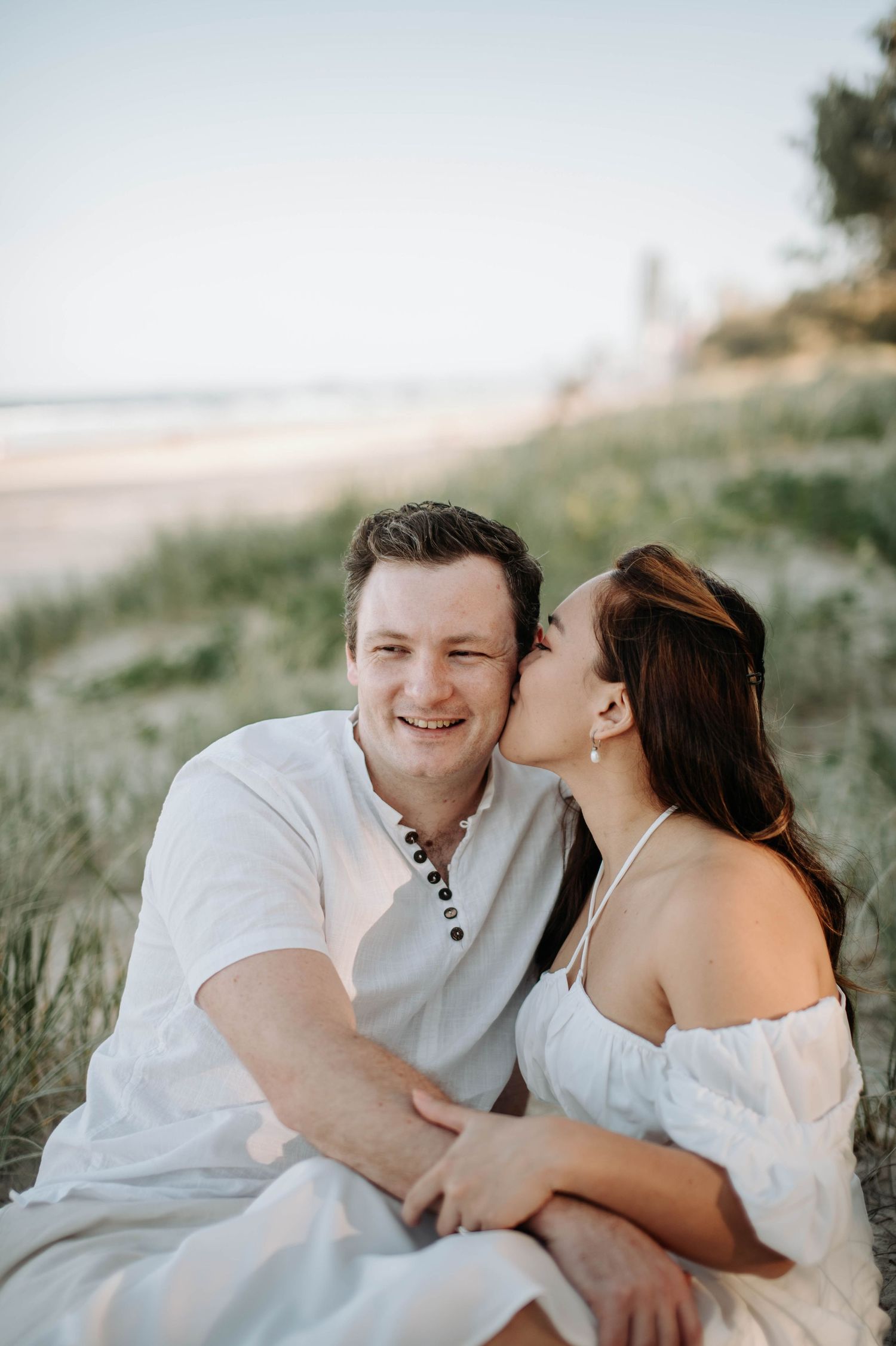 Casual beach engagement photo with couple sharing a tender moment by the ocean.