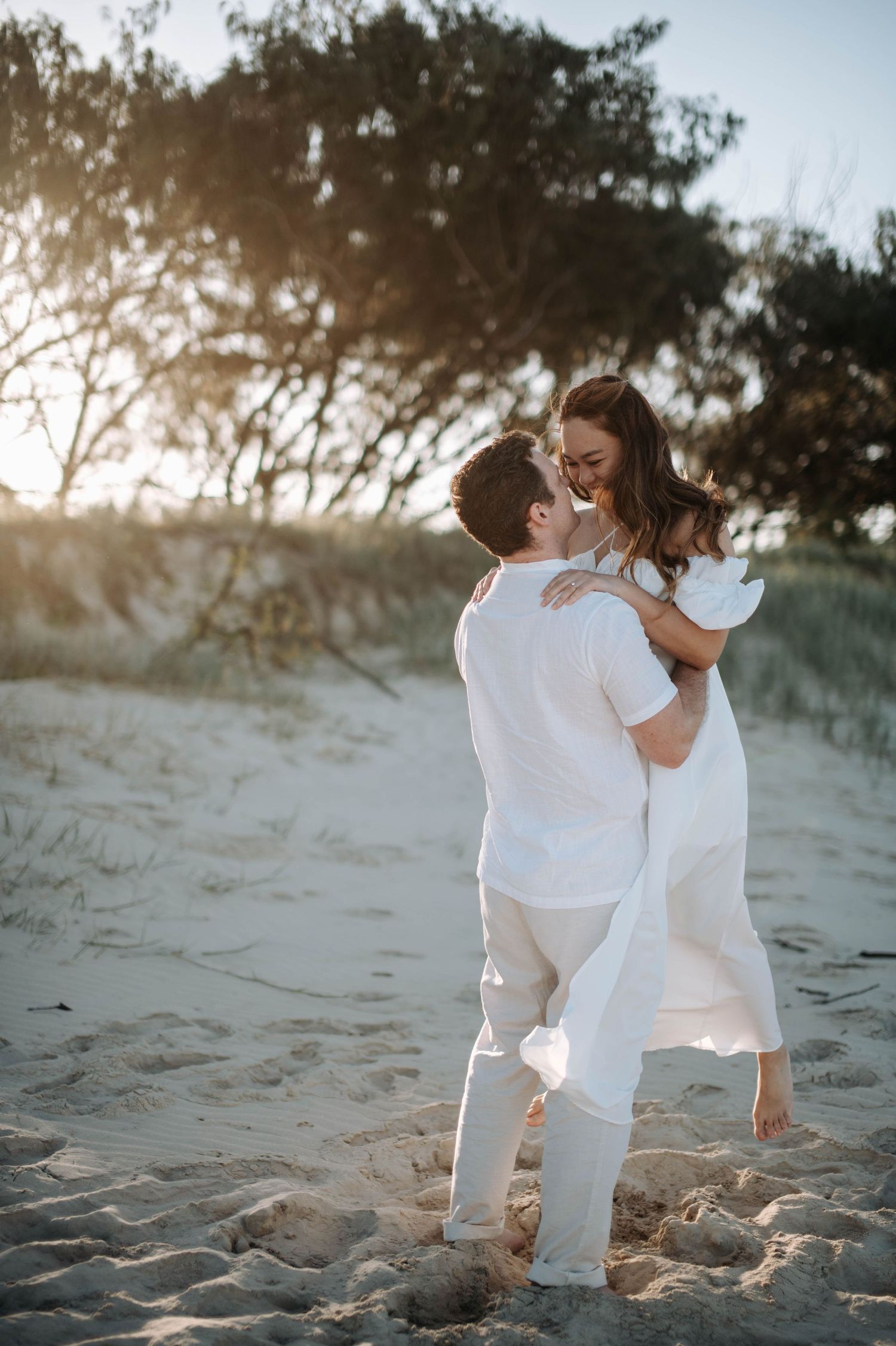 A couple shares a playful moment on the beach, with one person being lifted in the air.