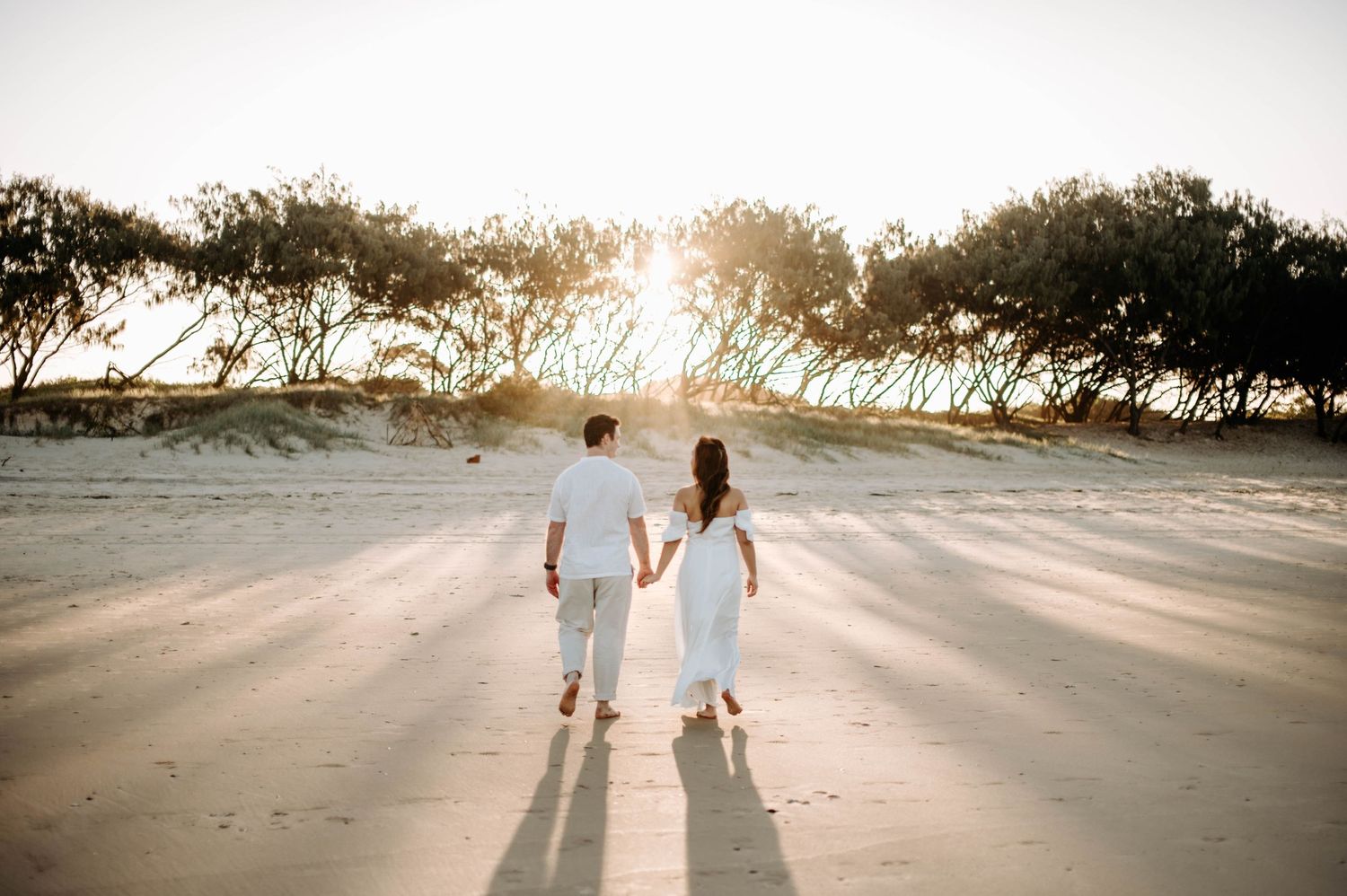 Silhouetted couple walking on beach during sunset with trees in background.