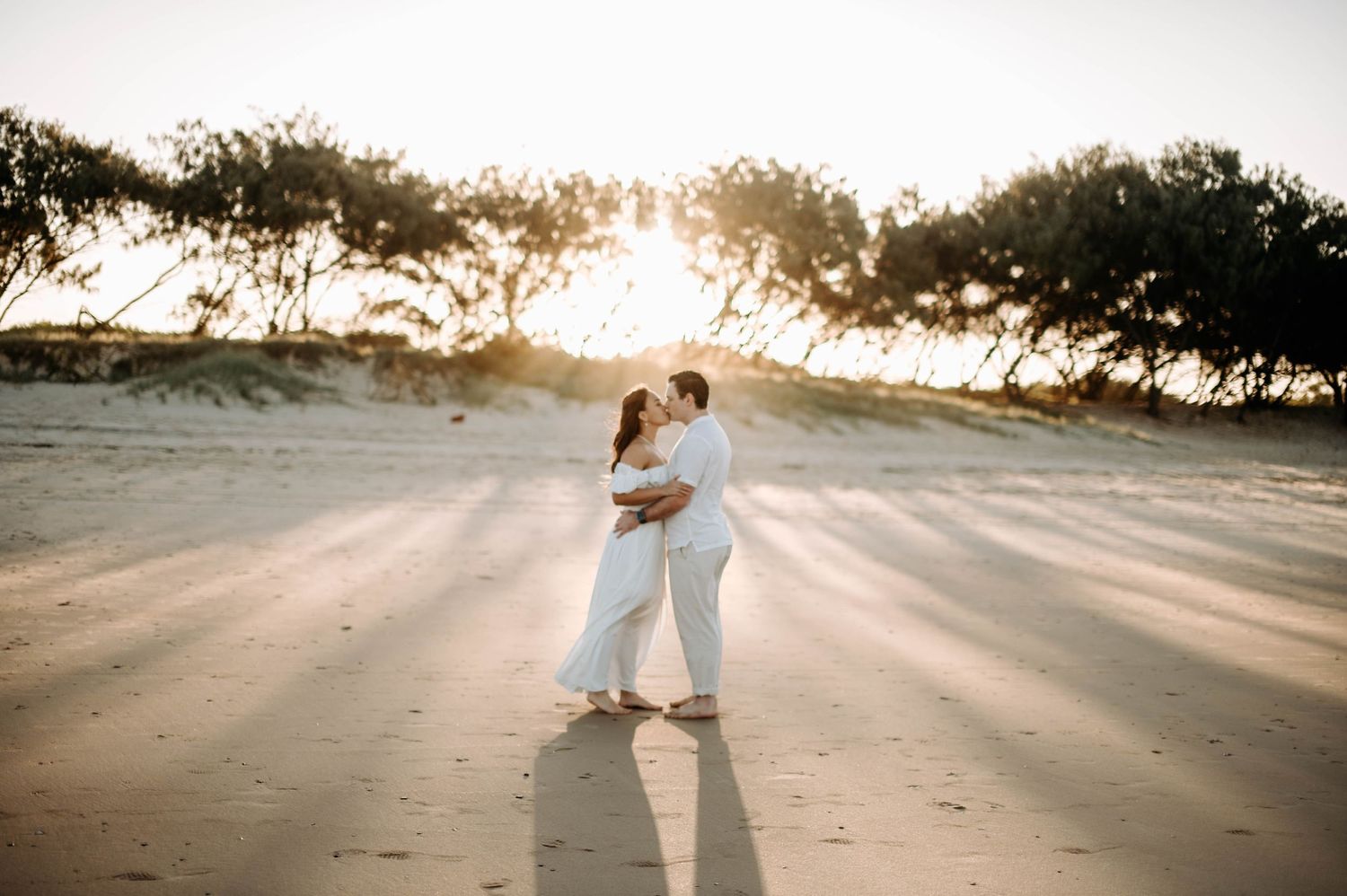 Romantic beach photo at sunset with couple embracing against golden light.
