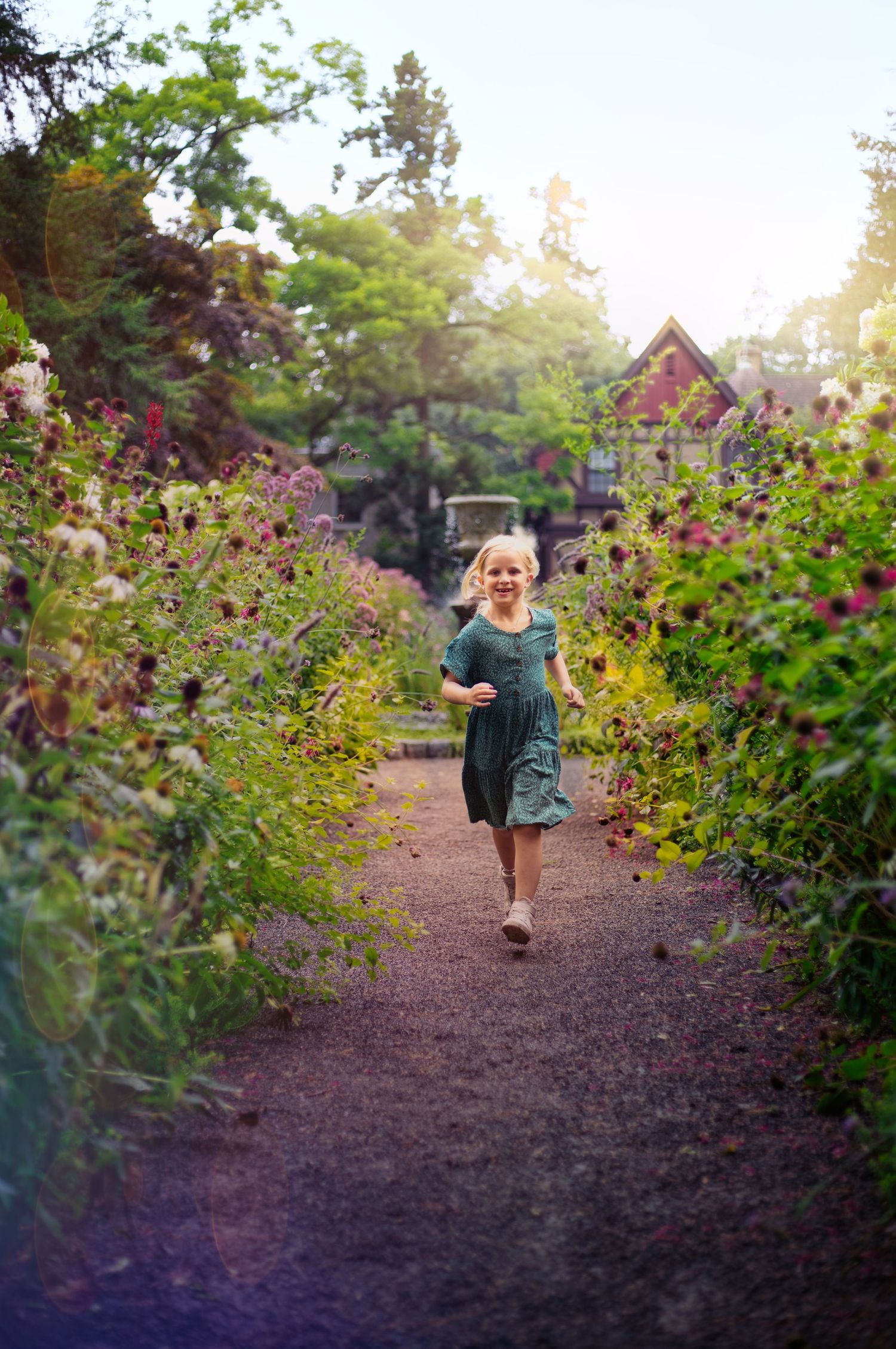 Child in dress running along garden path lined with colorful blooming flowers and rustic buildings.