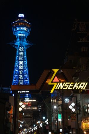 Blue illuminated tower and neon signs in a Japanese shopping district at night.