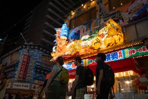 Bustling night market in Japan with illuminated signs and decorative lanterns.