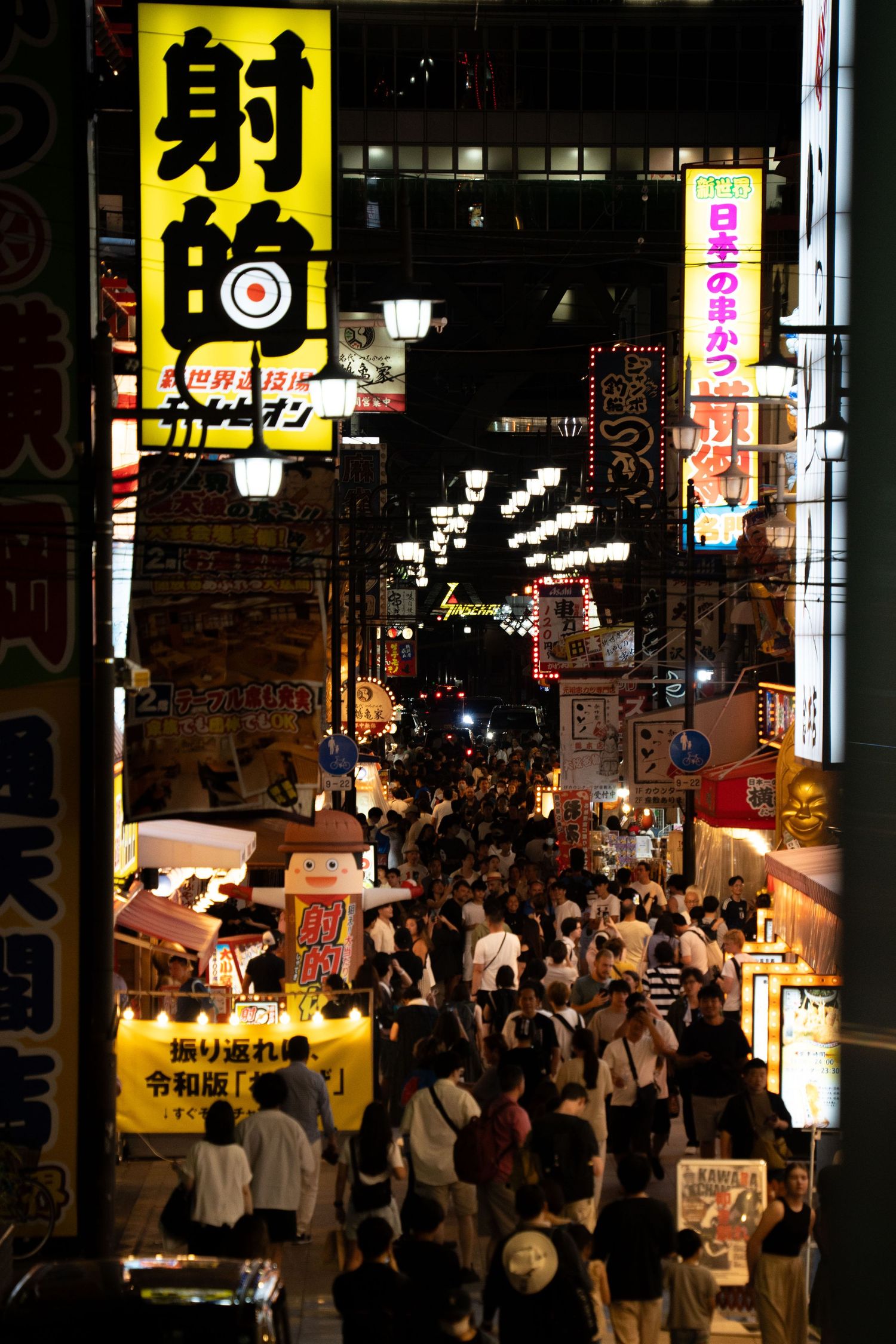 Crowded Japanese street at night with bright yellow signage and neon lights.