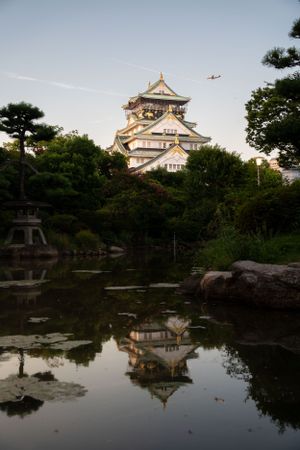 Japanese castle reflecting in a tranquil pond during sunset.
