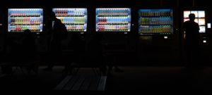 Row of bright digital displays glowing in a dark room showing information screens.