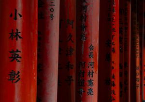 Red torii gates with Japanese characters and calligraphy in traditional shrine setting.