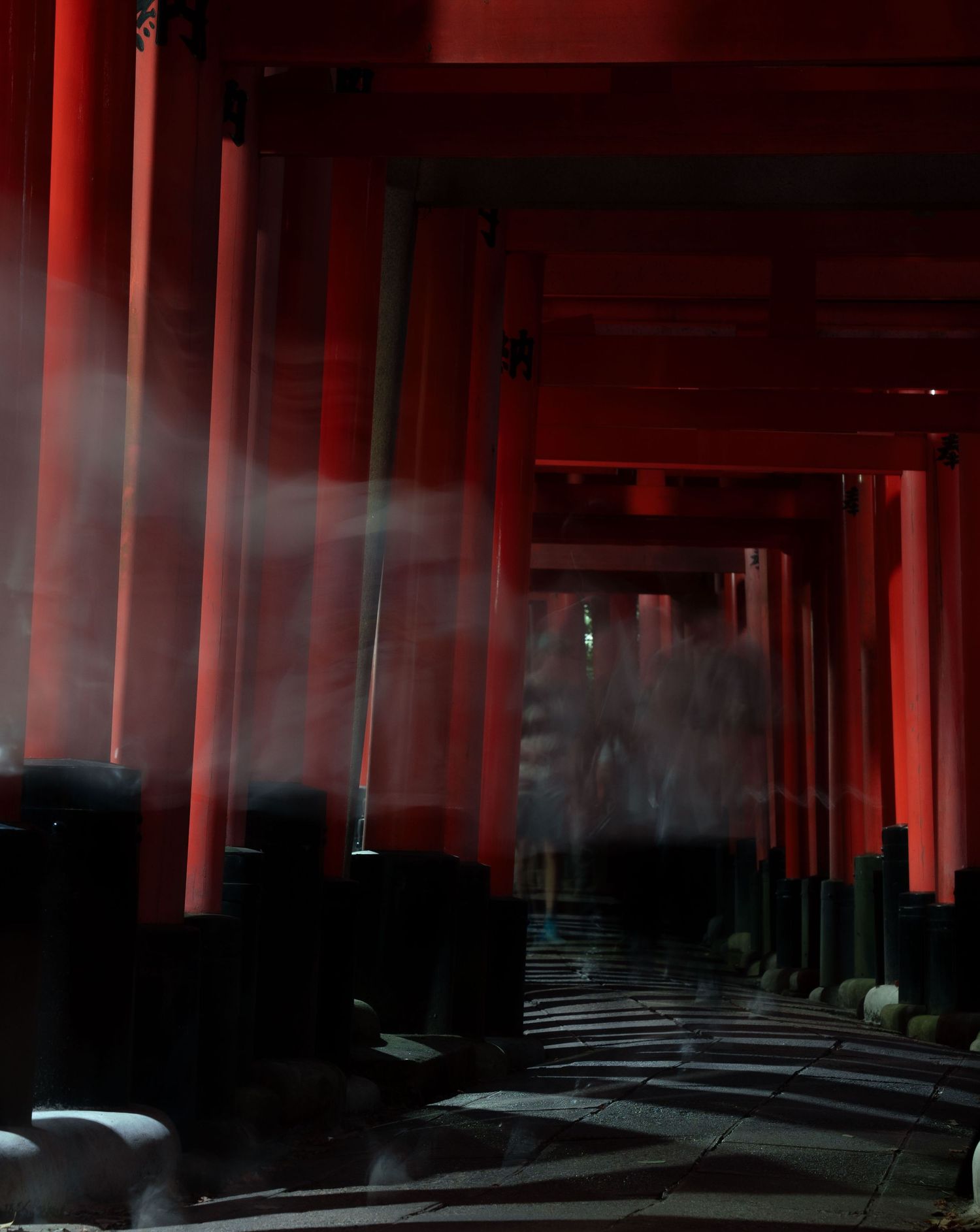 Long corridor of vermillion torii gates casting dramatic shadows at Fushimi Inari shrine.