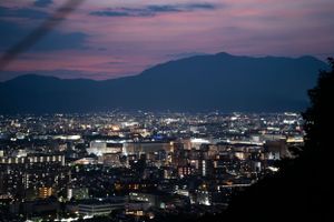 Panoramic cityscape of Kyoto at dusk with mountains and twinkling lights in the distance.